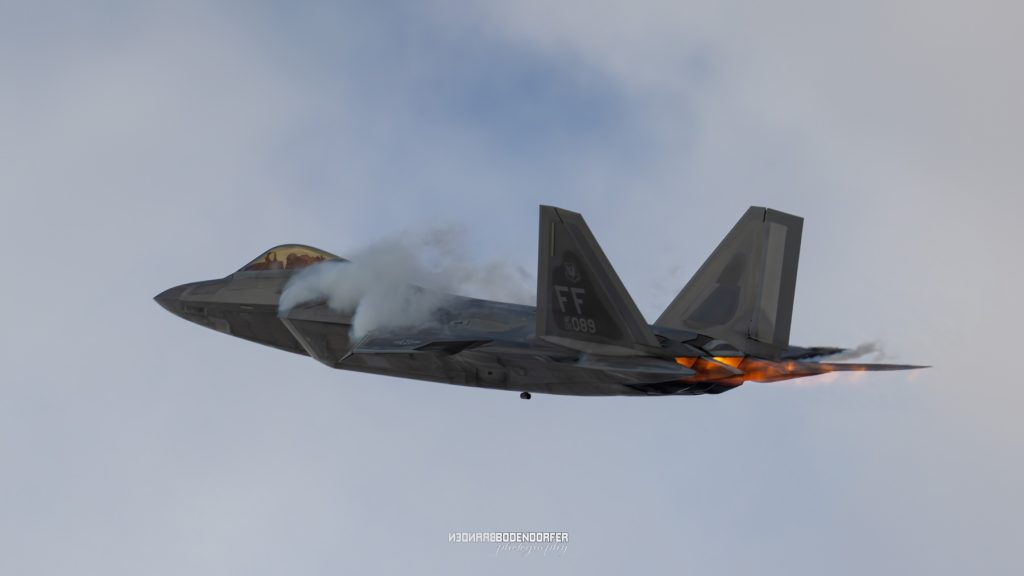 2024 EAA AirVenture Oshkosh Air Show Schedule 1 F-22 Raptor fighter jet with afterburners glowing during a pass at EAA AirVenture Oshkosh